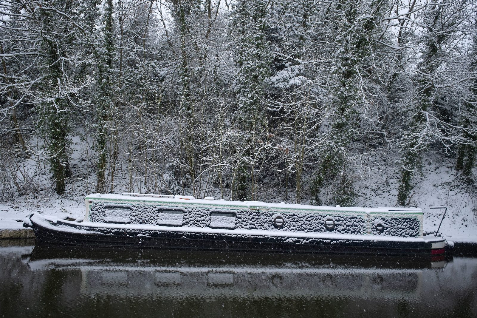 Canal boat with snowy trees behind it.